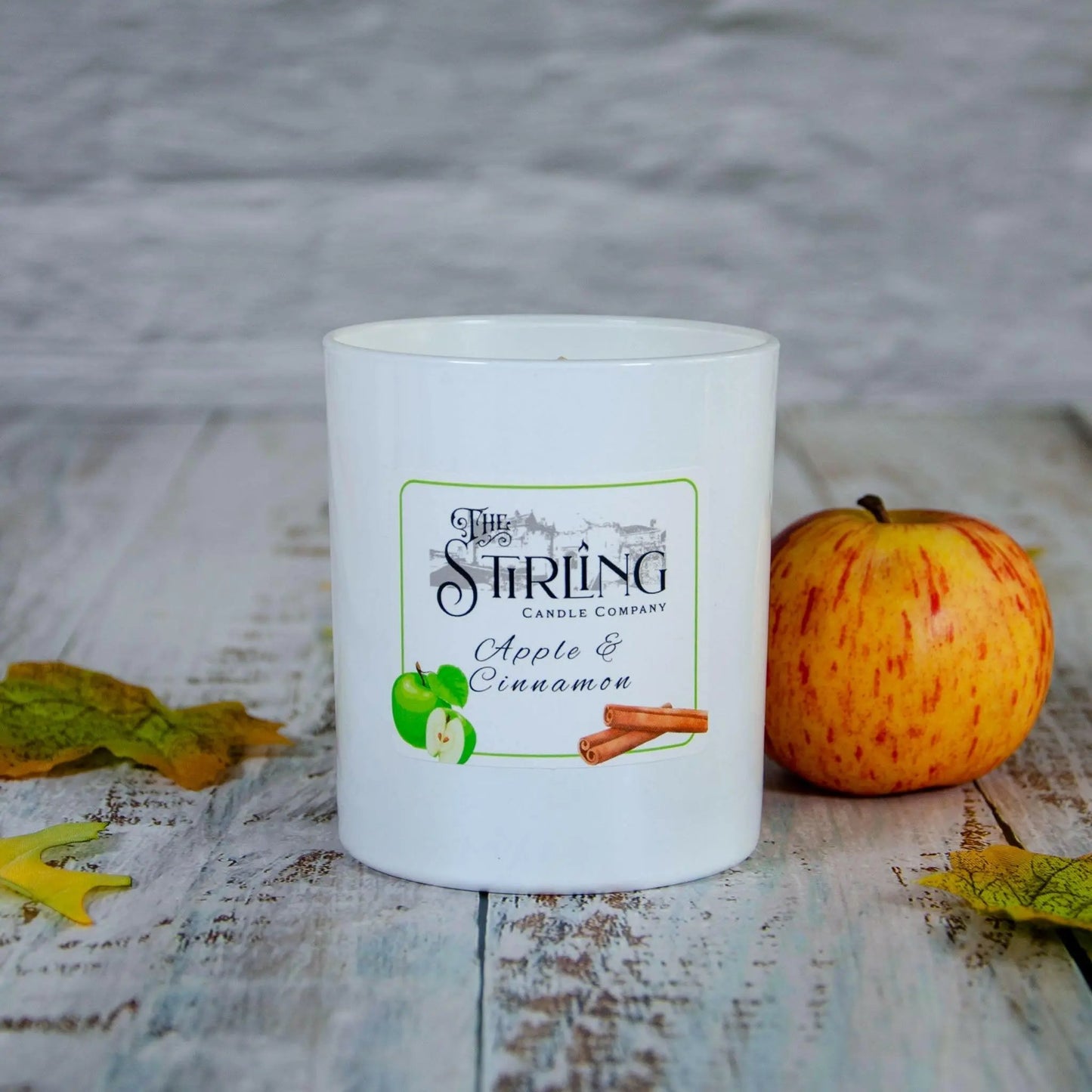 Large Apple & Cinnamon candle from Stirling Candle Company next to a red apple and autumn leaves on wood