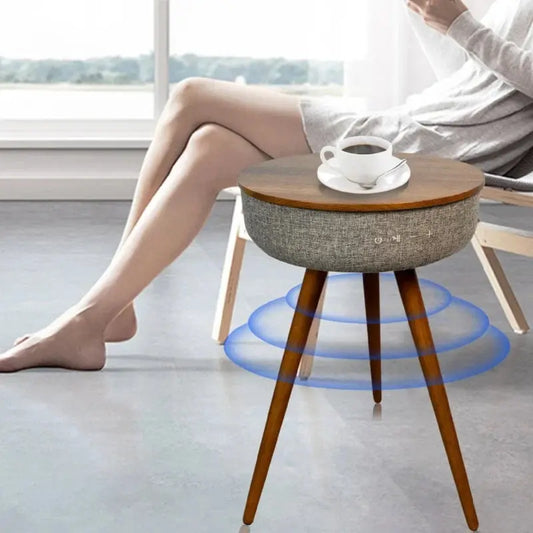 Round smart coffee table with wooden top, grey fabric speaker, and wood legs, next to a person with coffee cup.