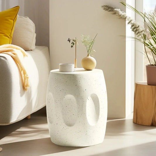 Modern round lightweight concrete side table with textured indents, next to a sofa in a living room.
