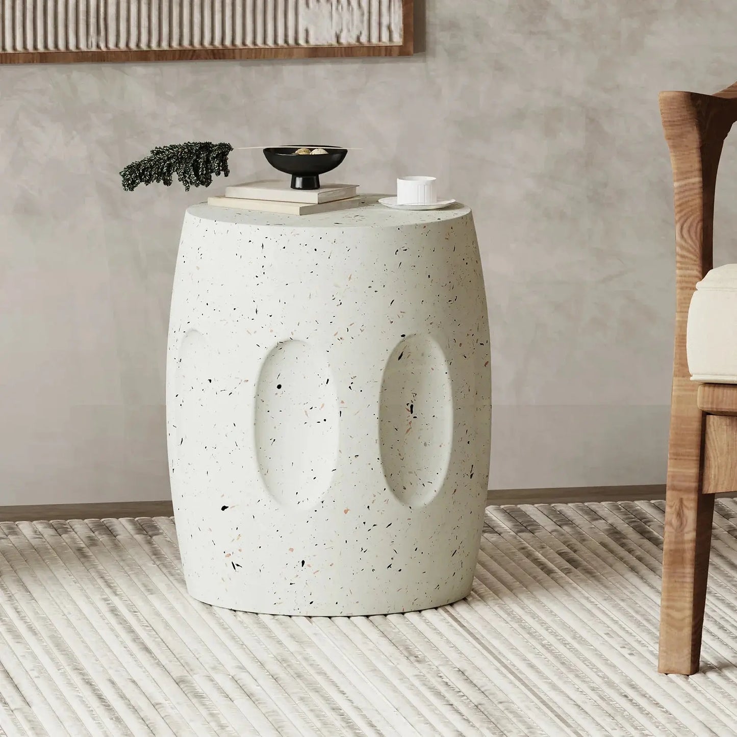 Modern round concrete side table with terrazzo flecks, featuring books, black bowl, and teacup in a minimalist living room.