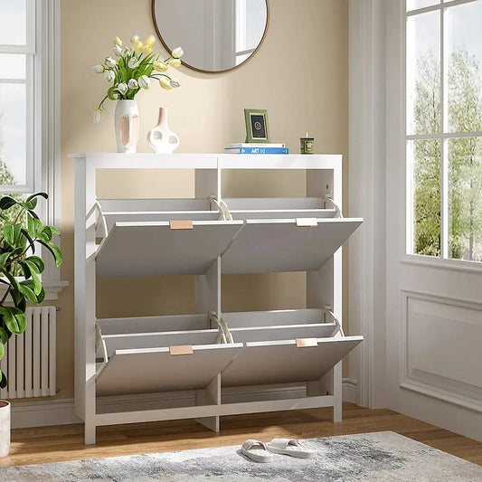 White flip-down wood shoe cabinet with 4 open shelves in an entryway, slippers on rug, plants beside.