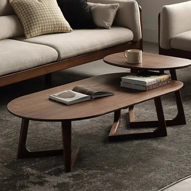 Modern wooden coffee table set in a living room, with an oval lower table and a smaller oval upper table