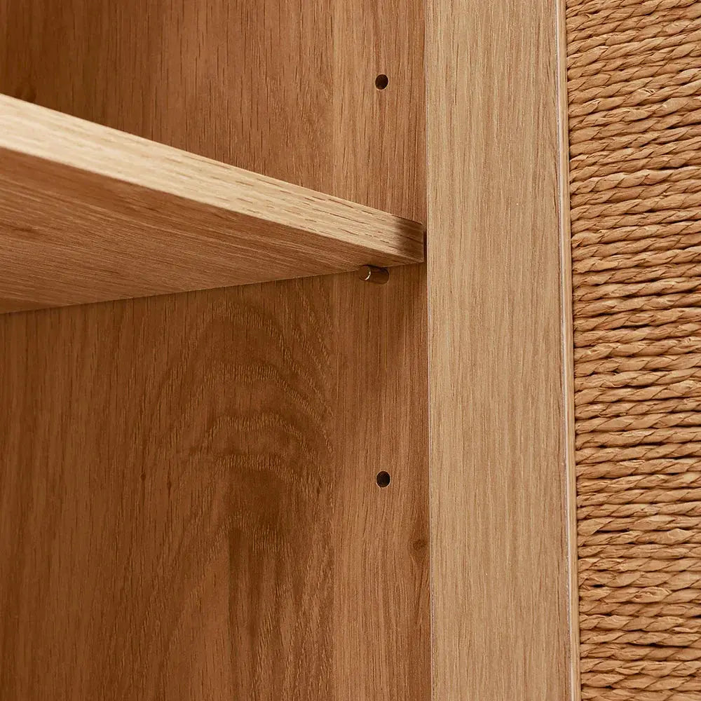 Close-up of wooden sideboard interior with a shelf supported by pegs, next to a woven rattan door panel