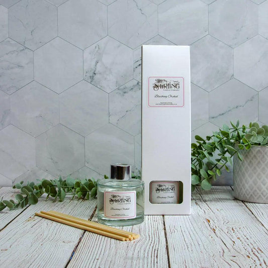 Blushing Orchid 100ml luxury reed diffuser, box, and reeds on wood surface with plants and hexagonal tiles