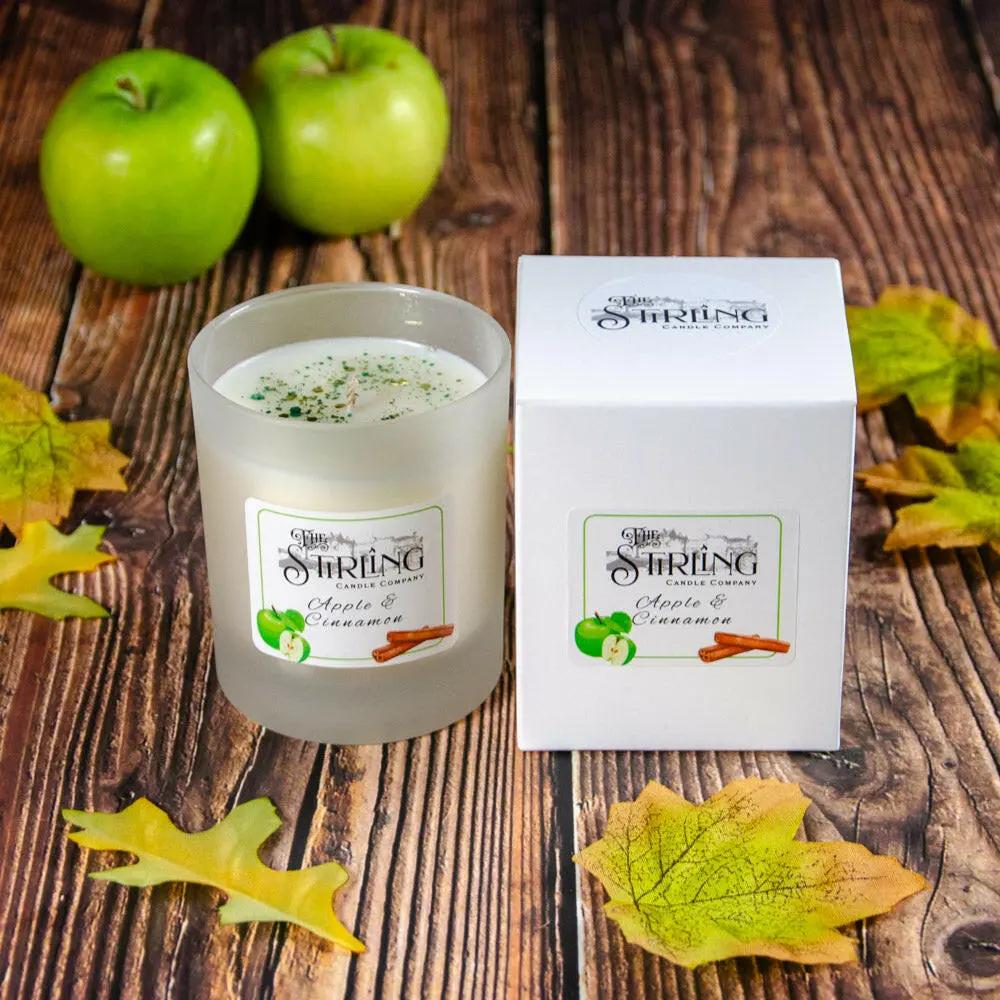 Apple & Cinnamon medium candle in frosted glass with white box, green apples, and autumn leaves on wood.