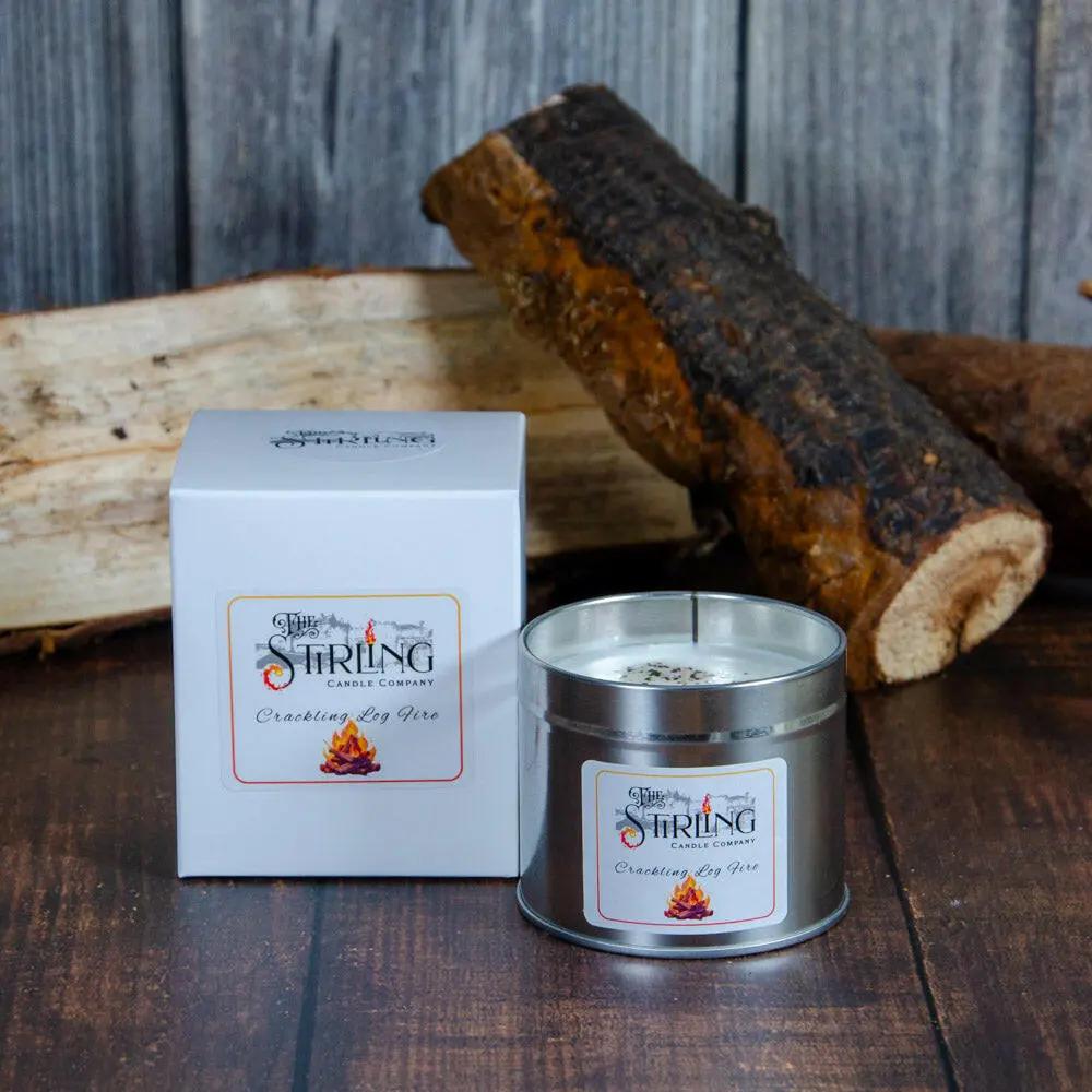 Crackling Log Fire Travel Tin Candle with box and cotton wick, beside logs on wood.