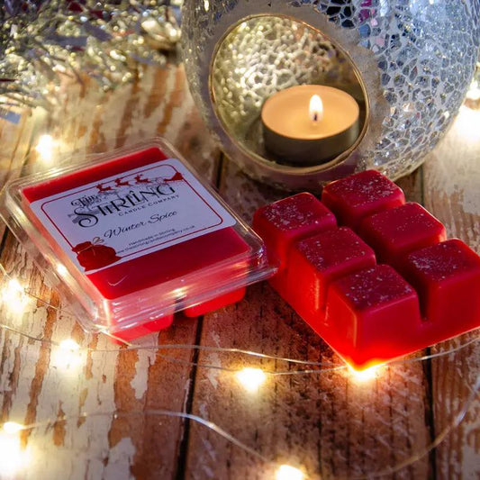 Red Winter Spice wax melt clamshell & six wax cubes beside a lit tealight in a mosaic burner with fairy lights.