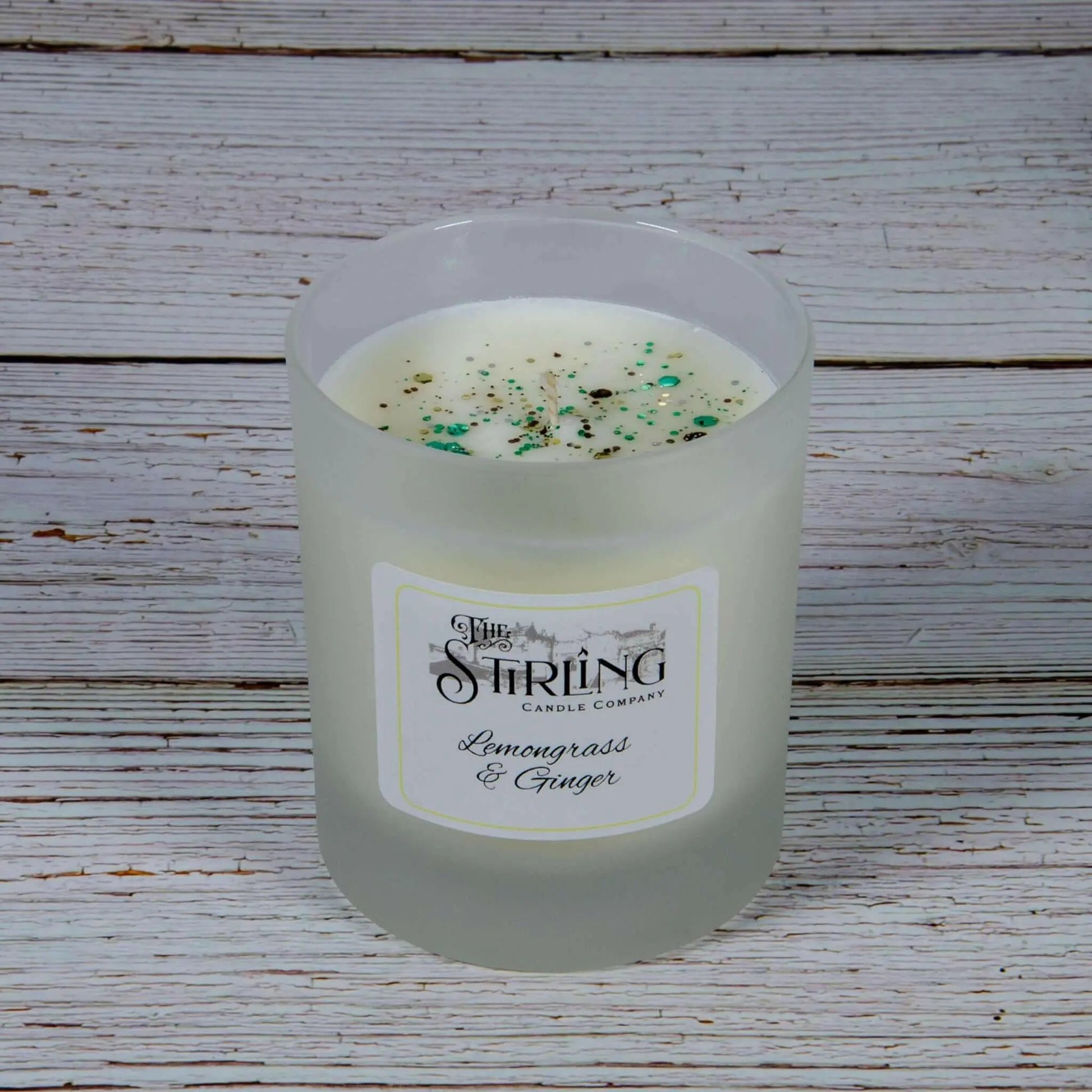 Lemongrass & Ginger medium candle in a frosted glass jar with white wax and green and brown speckles on white wooden background