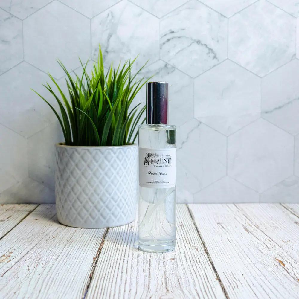 Fresh Start 100ml room spray bottle next to a potted green plant on a light wooden surface