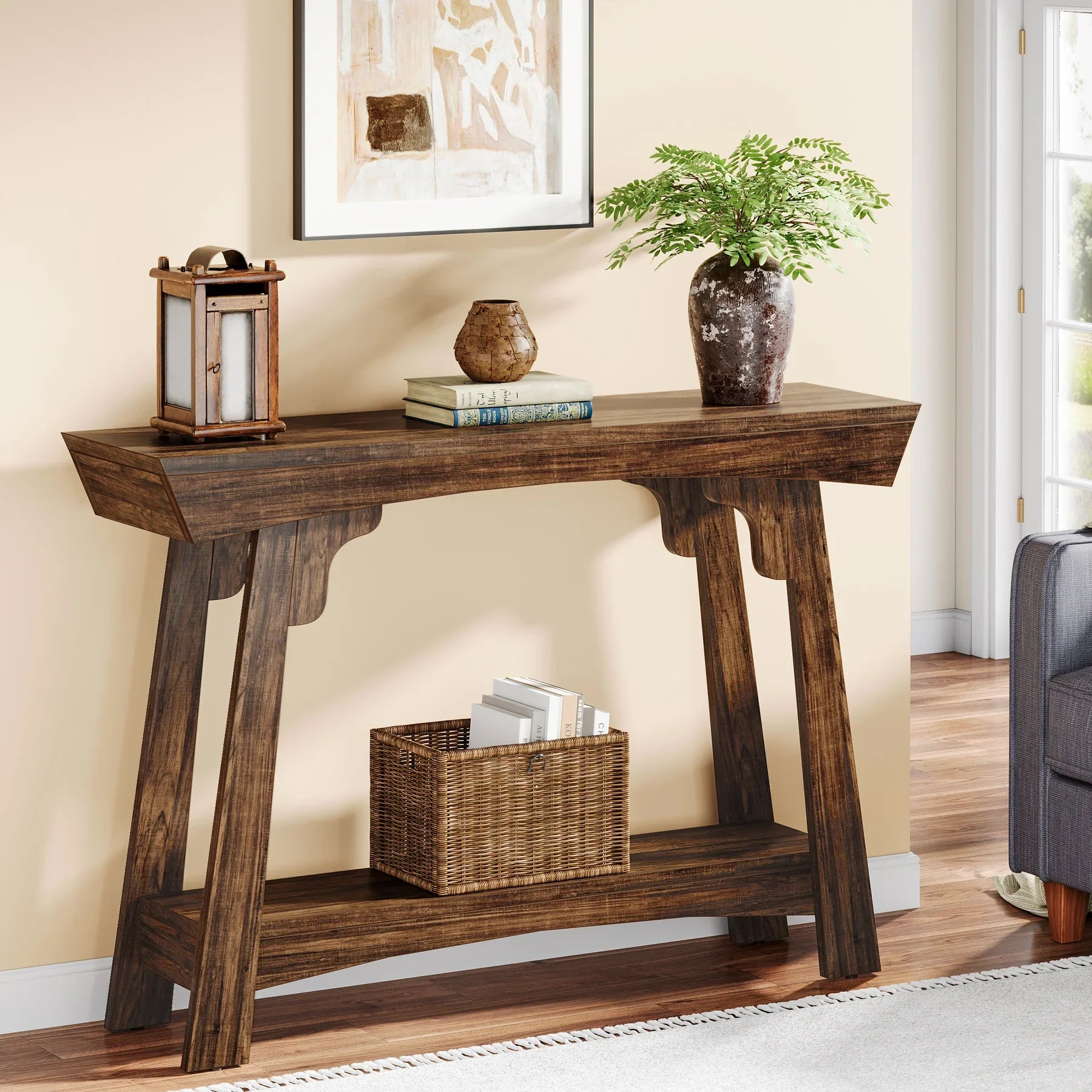 Rustic brown 2-tier entryway table with decorative lantern, books, and green plant on top; wicker basket on bottom shelf