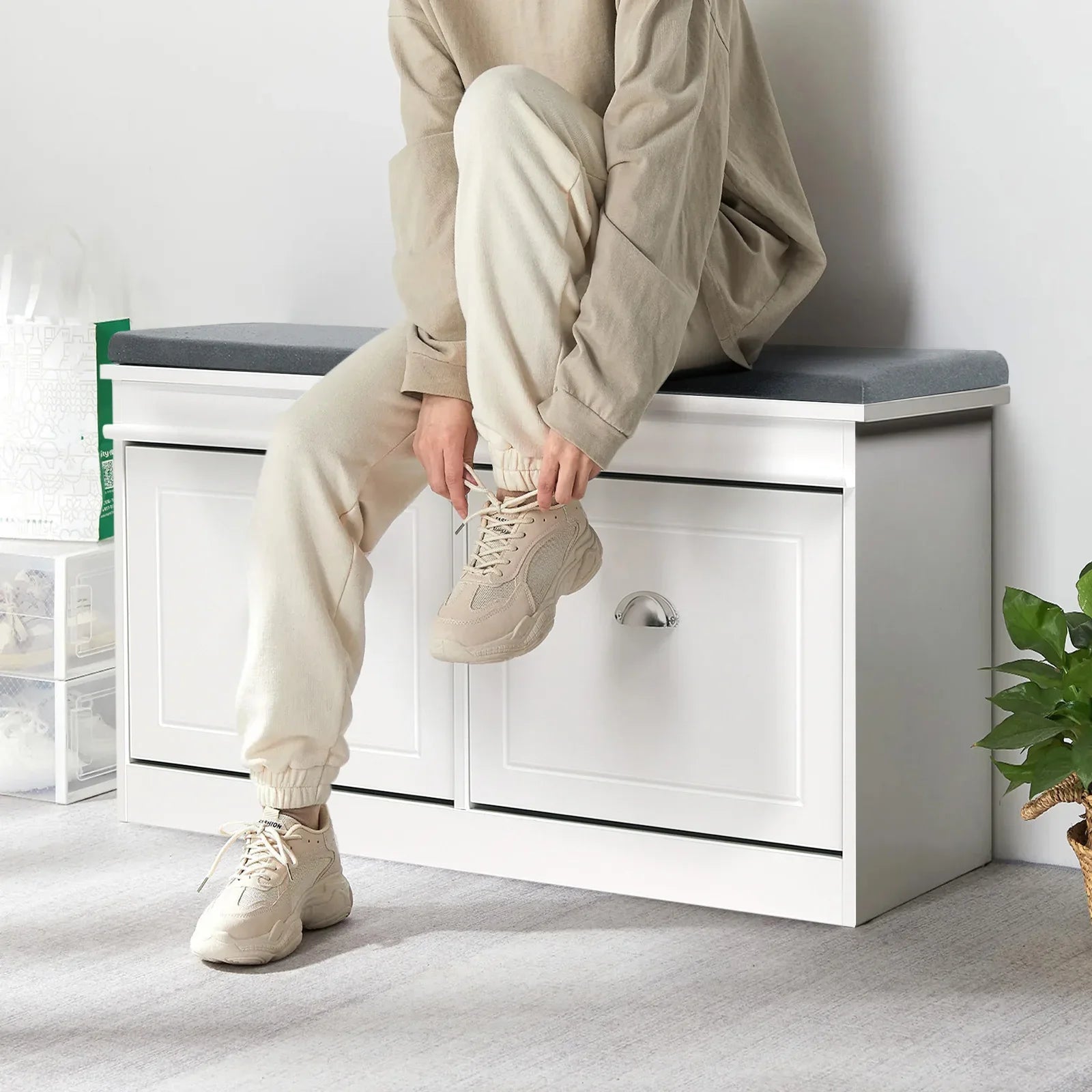 Person tying shoelaces on a white flip-top shoe cabinet with a grey cushion, ideal for entryway shoe storage.