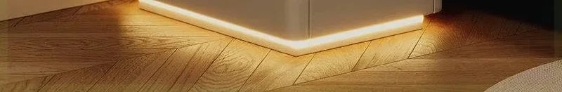 Close-up of a modern white nightstand with a subtle LED light strip illuminating the wooden floor below it.