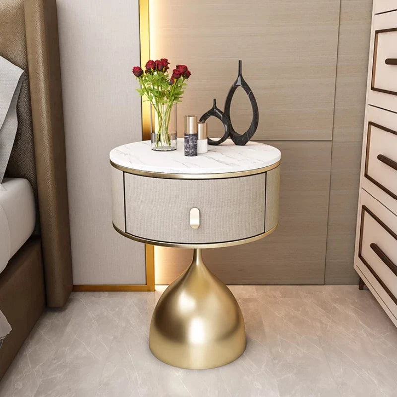 Luxury unique gold nightstand with marble top, fabric drawer, and sleek gold base, next to a bed.