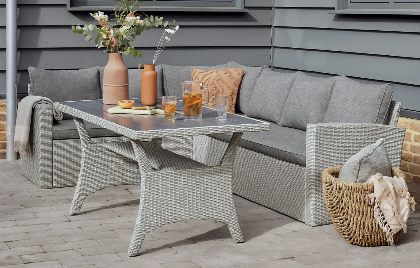 Stockholm 6 Seater Grey Rattan Corner Garden Dining and Lounge Set with grey cushions, table, and decor.