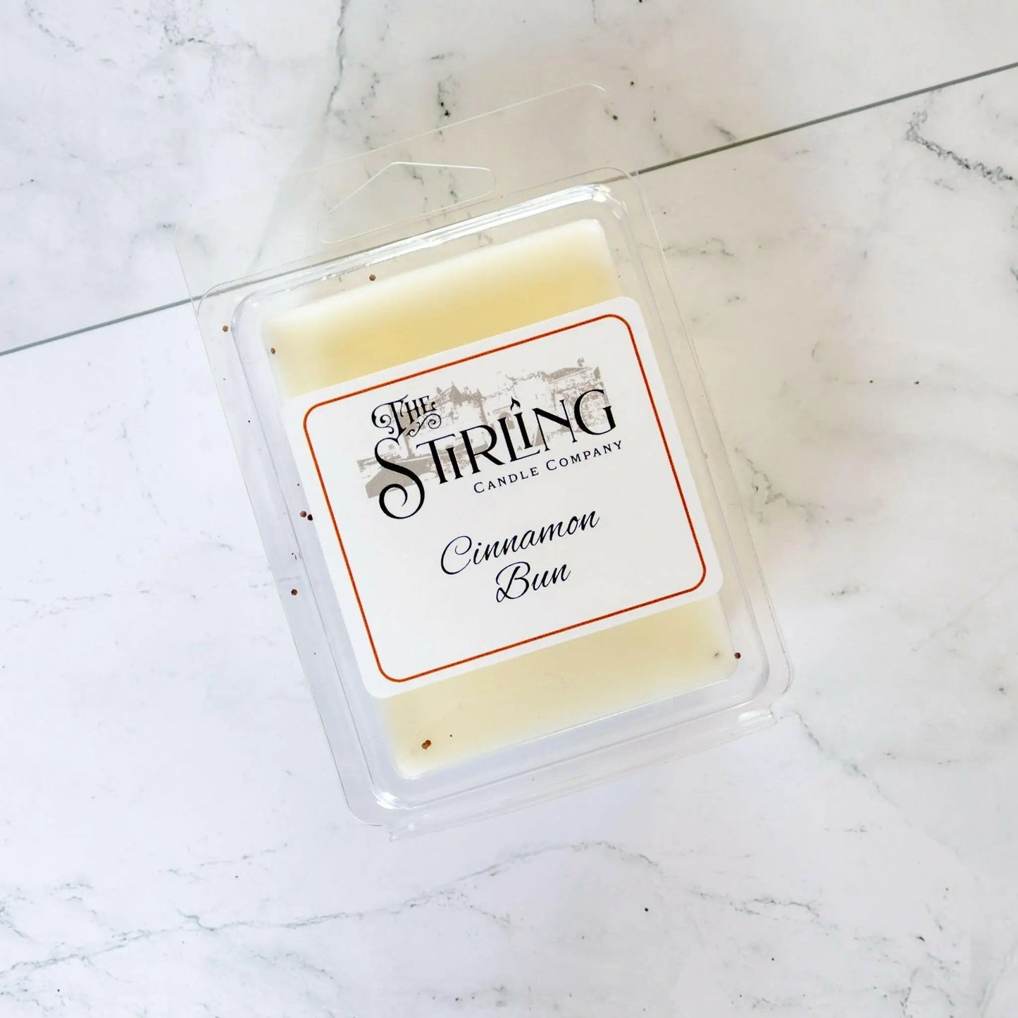 Cinnamon Bun wax melt clamshell by The Stirling Candle Company, shown in clear packaging on a white marble surface