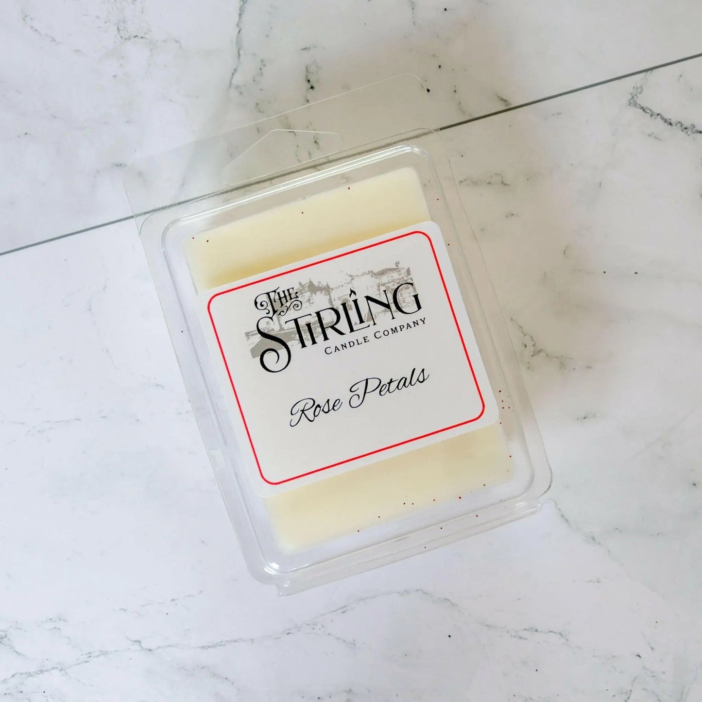 Rose Petals wax melt clamshell by The Stirling Candle Company, off-white wax with red glitter on a marble background.