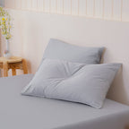 Gray pillows on a bed with a wooden side table and flowers in the background