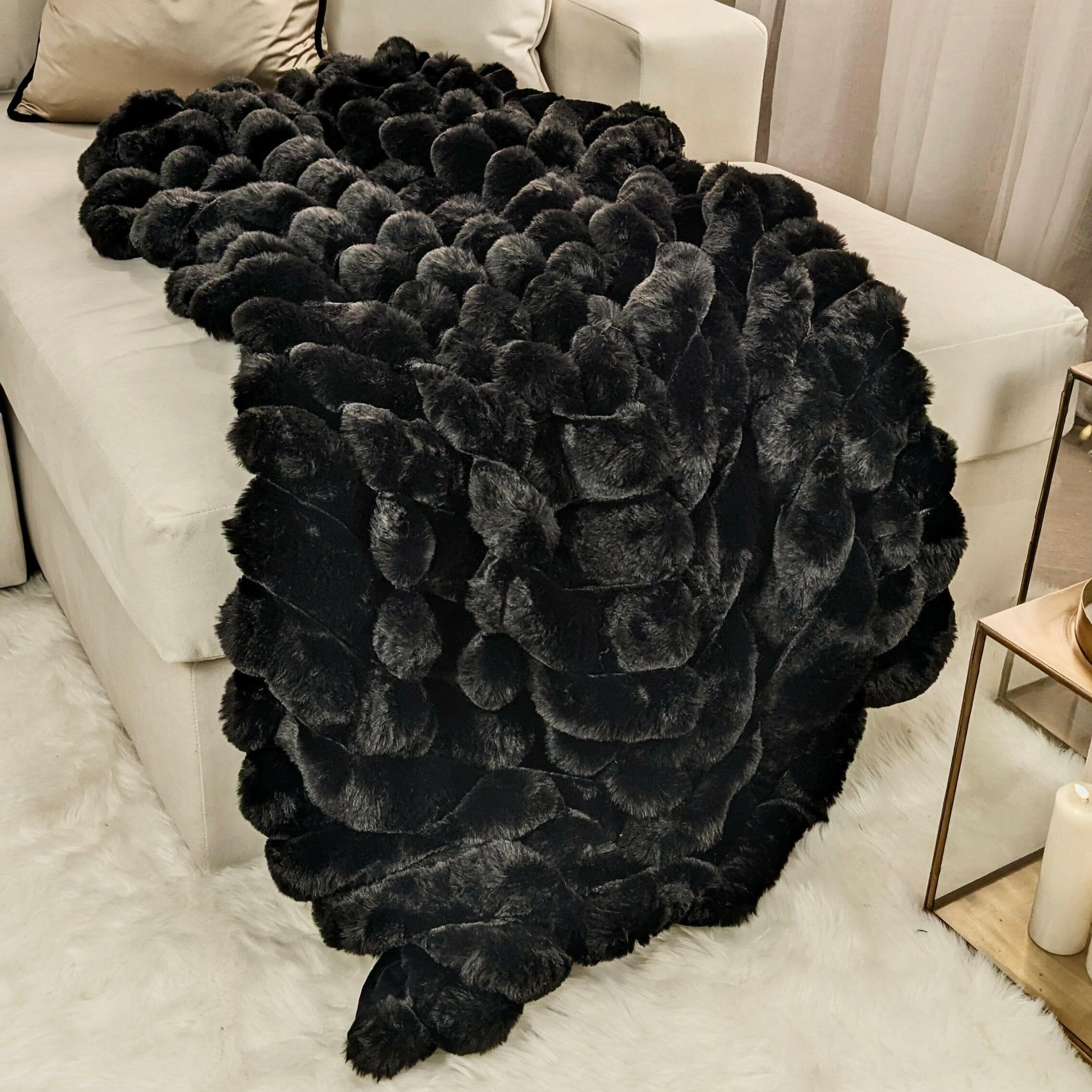 Isla black chunky ribbed faux fur throw draped over a cream sofa, with a cream rug and white candles