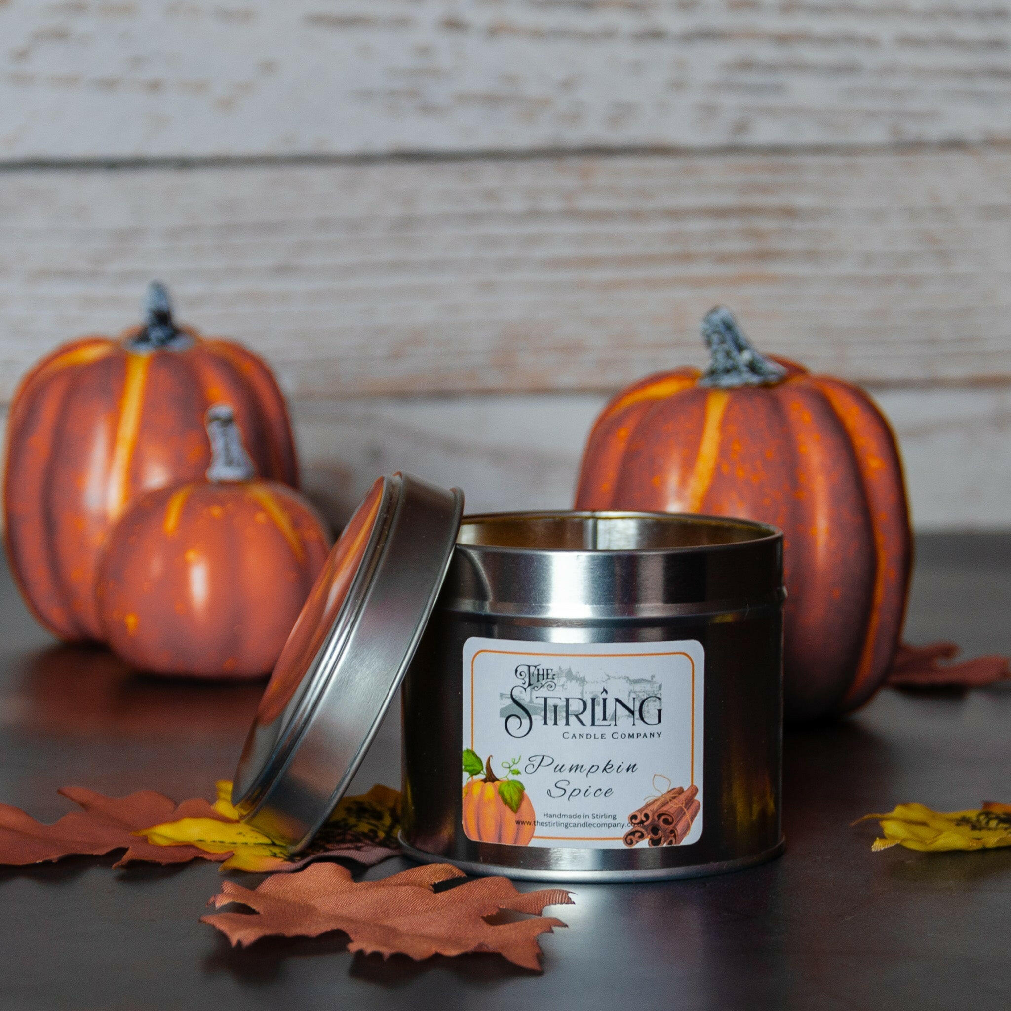 Pumpkin Spice Travel Tin candle, lid ajar, with autumn pumpkins and leaves in background for a cosy feel.