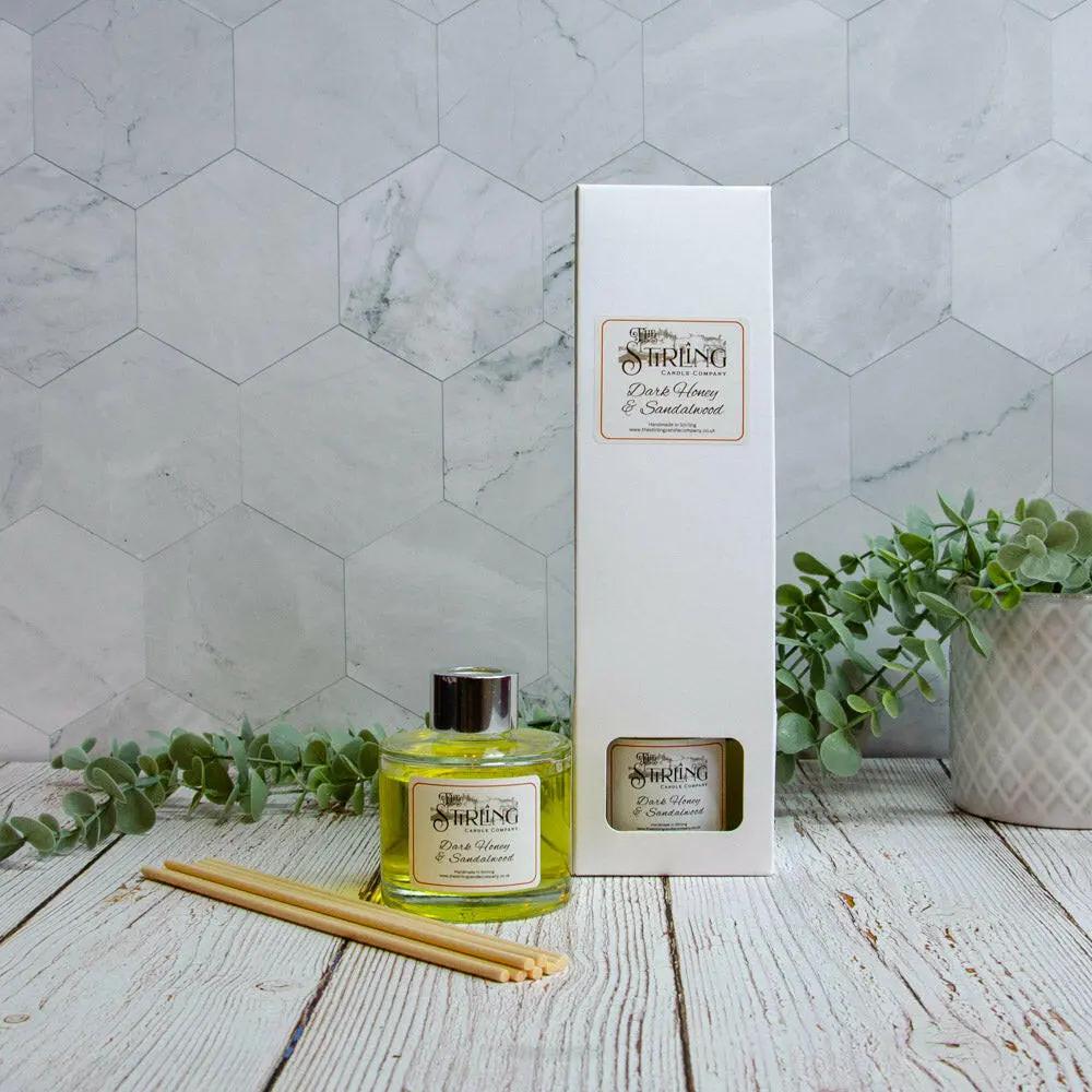Dark Honey & Sandalwood 100ml diffuser, reeds, and packaging box on a wooden surface with plants.