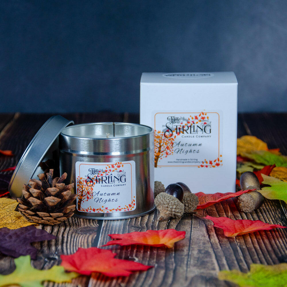 Autumn Nights travel tin candle and white box on wood, surrounded by autumn leaves, pinecone, and acorns