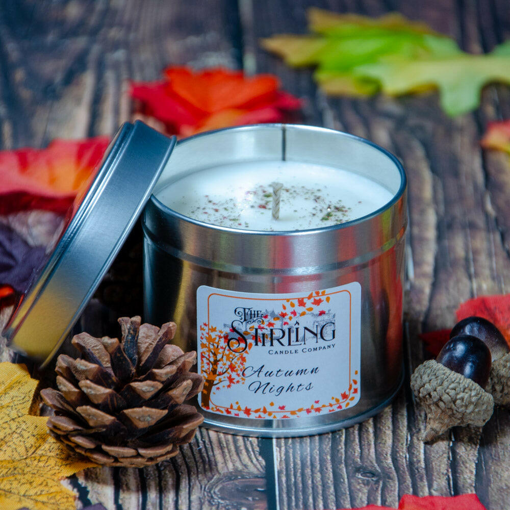 Autumn Nights Travel Tin Candle with cotton wick, lid open, pinecone, and acorns on wooden background