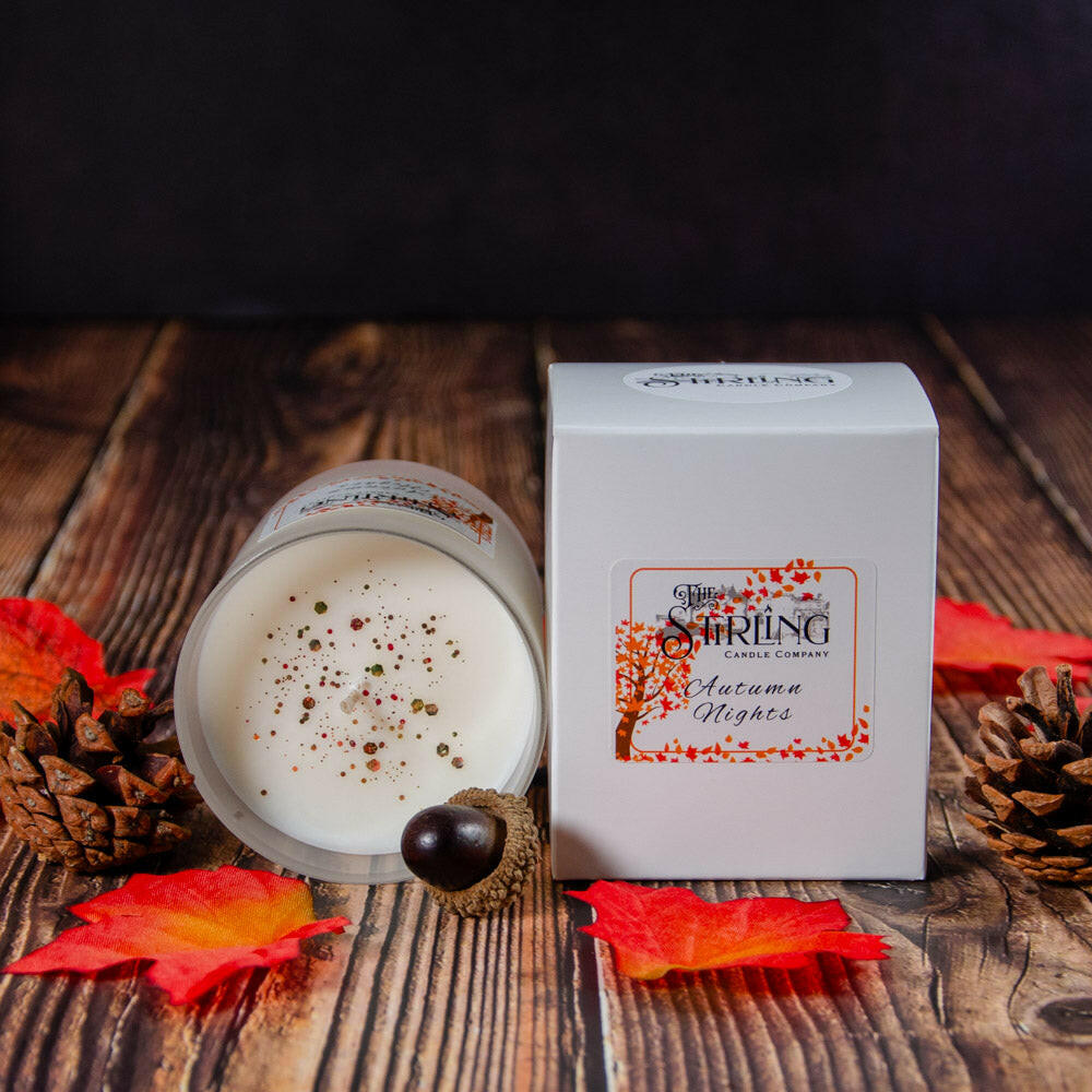 Autumn Nights Medium Candle with label and white box, showing glittery surface on wooden background.