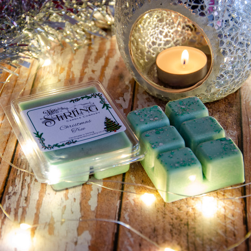 Christmas Tree wax melt clamshell & six green wax melt blocks with glitter. Tealight warmer & string lights create festive glow.
